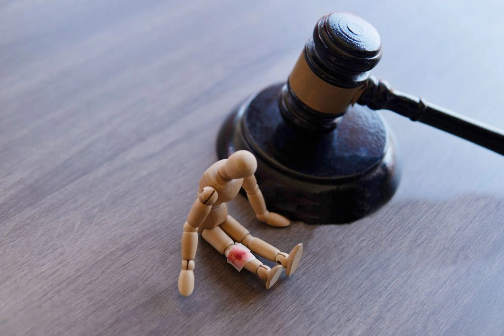 Victime d’un accident de la vie symbolisée par une figurine blessée au genou, placée devant un marteau de juge représentant l’indemnisation du dommage corporel.