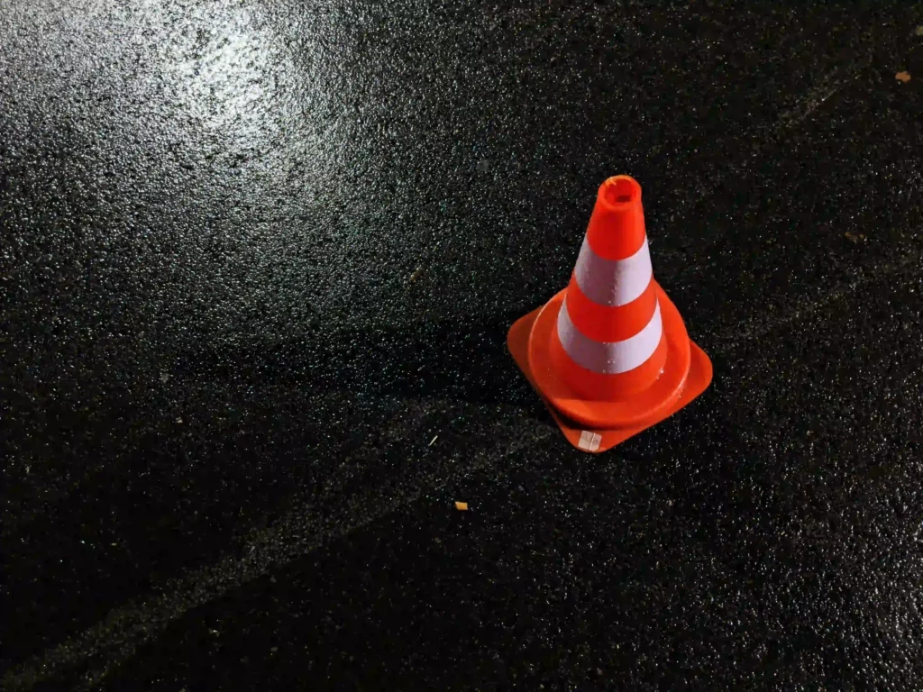 Cône de signalisation orange posé sur la chaussée mouillée après un accident de la route, utilisé pour sécuriser la zone.