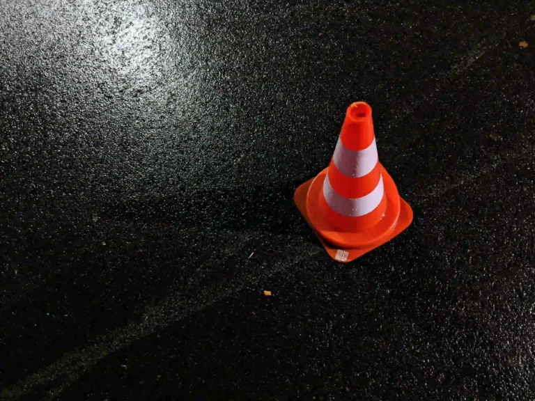 Cône de signalisation orange posé sur la chaussée mouillée après un accident de la route, utilisé pour sécuriser la zone.